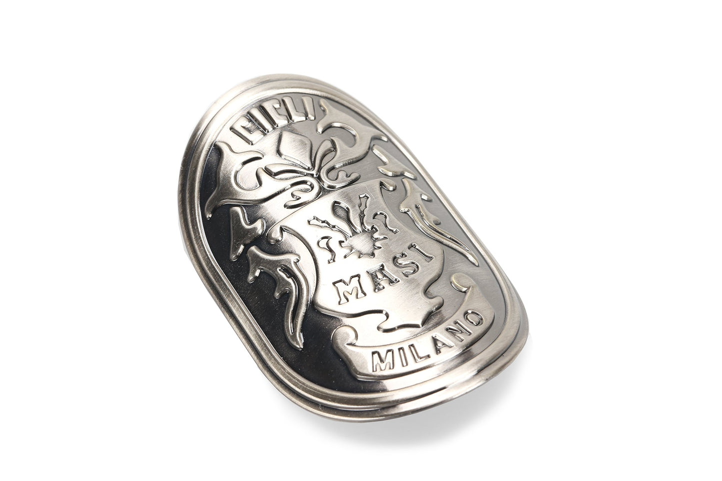 A silver oval keychain or badge by Masi Bikes, featuring ornate designs and the embossed text Masi Milano, with a central shield-like emblem, intricate patterns, and floral motifs. Product: MASI HEAD BADGE.