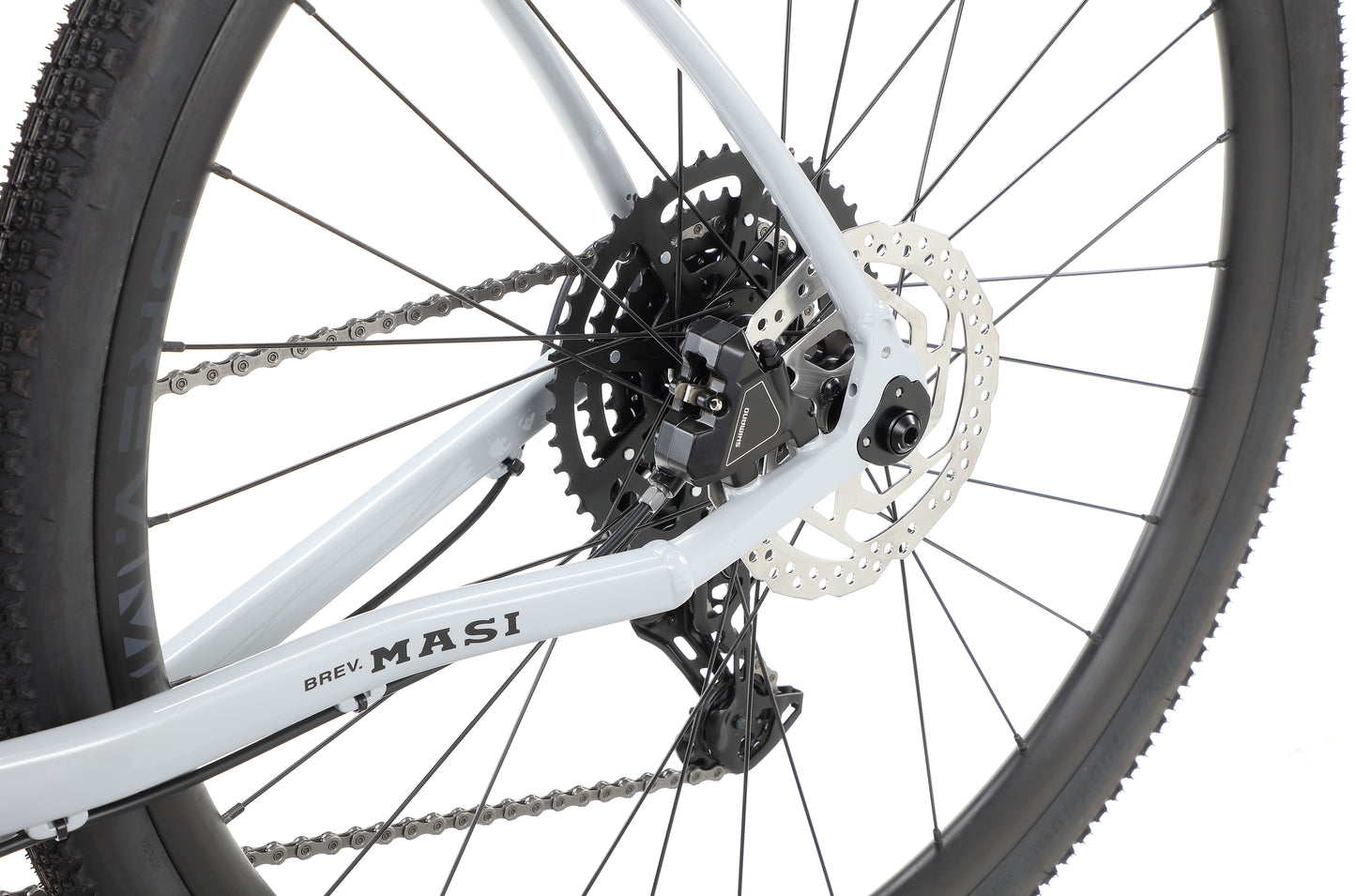 Close-up of a BRUNELLO 3 bicycles rear wheel with disc brake, gears, and part of the chain on a white Masi frame.