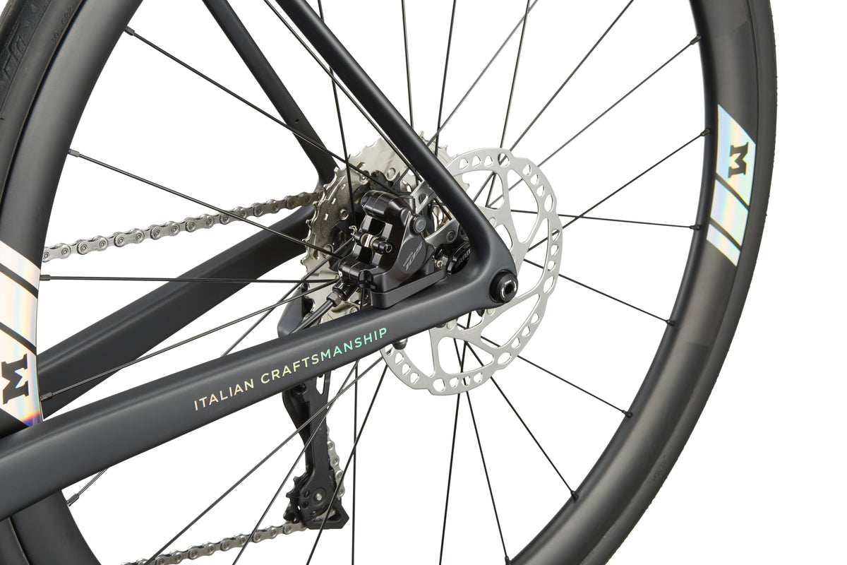 Close-up of the GRAN CORSA carbon road bike’s rear wheel, disc brake, chain, and Italian craftsmanship on the frame.