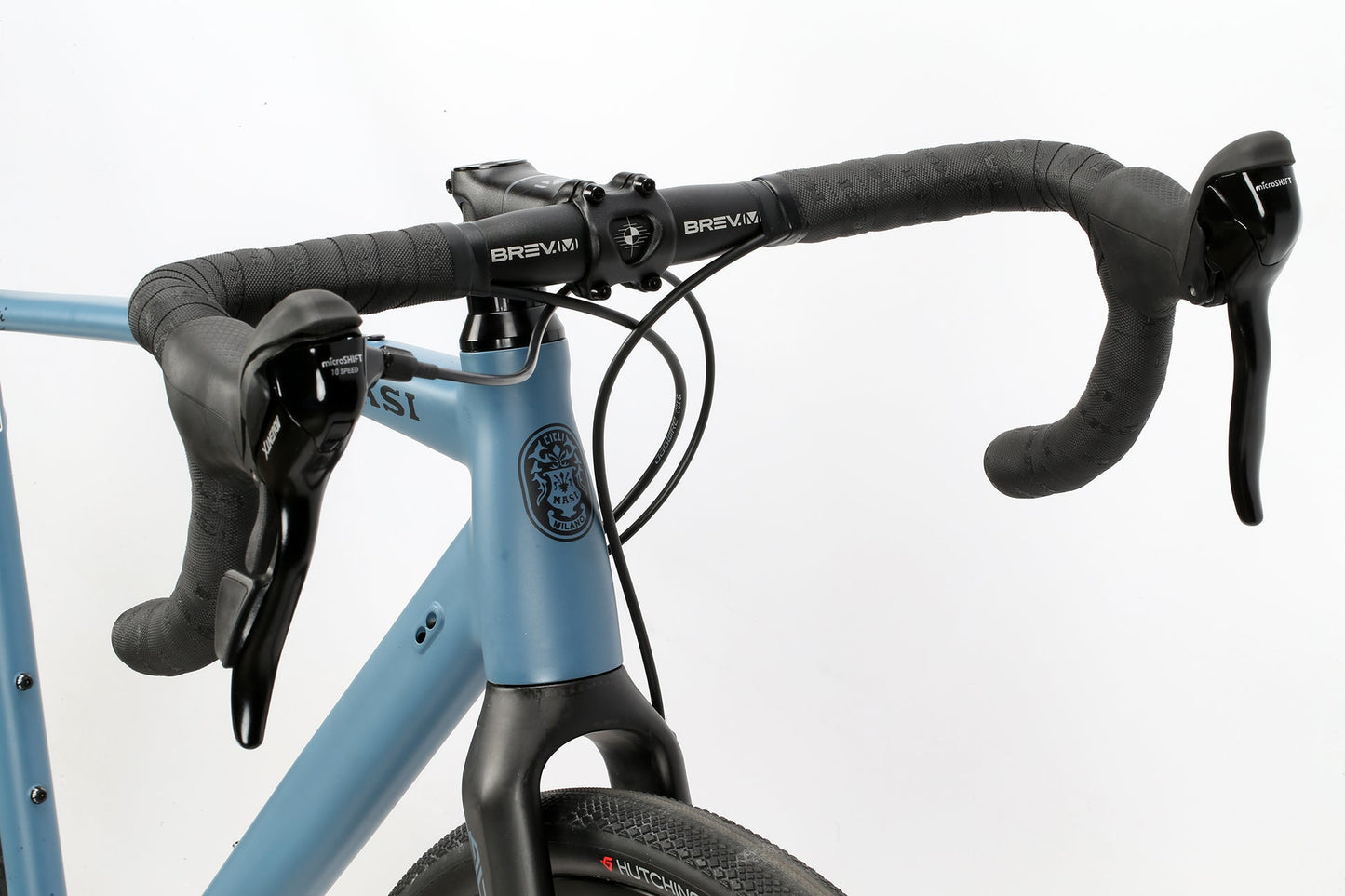 Close-up of BRUNELLO ADX road bikes handlebars with black grips, gear shifters, a blue frame, full carbon fork, and front brake cable.
