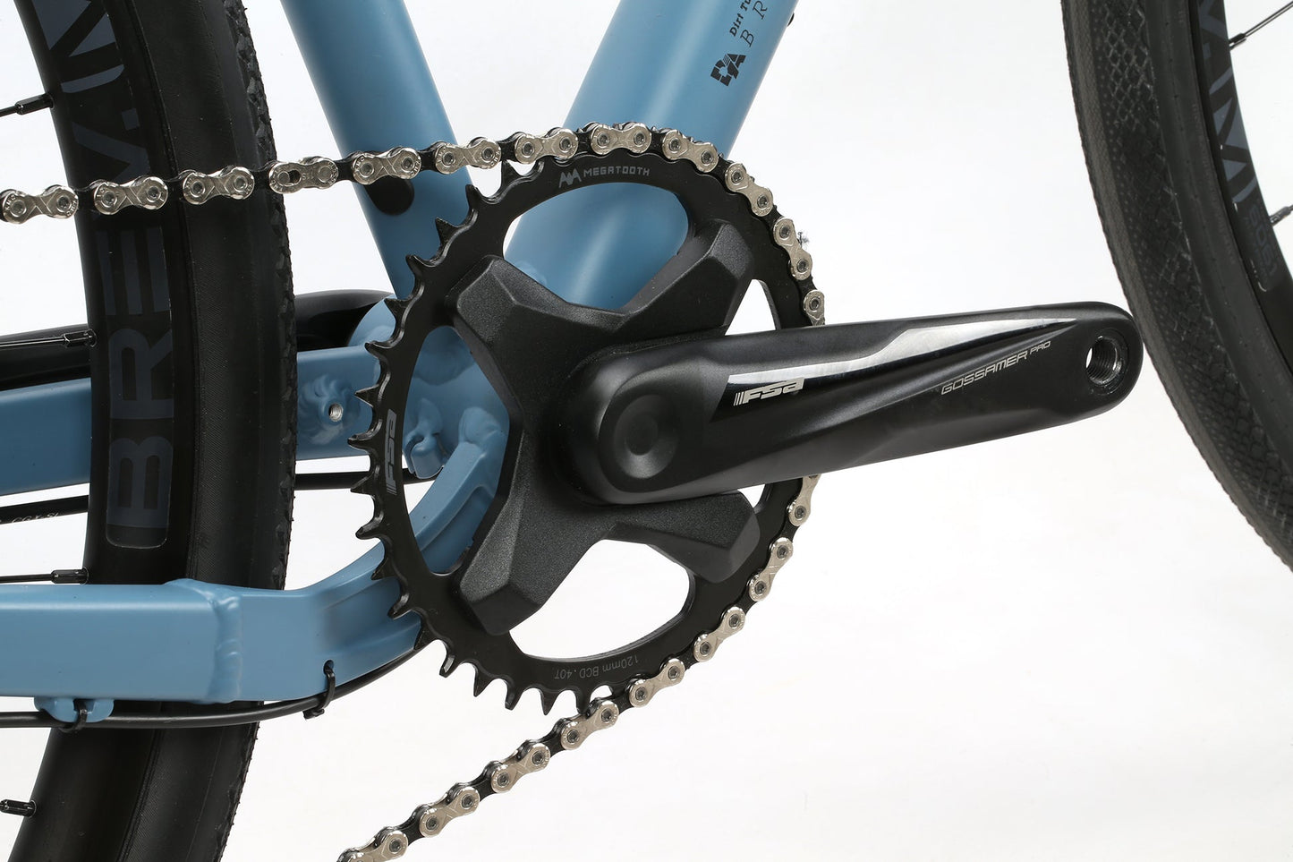 Close-up of the 1X drivetrain and chain on BRUNELLO ADXs blue aluminum gravel frame with black crank arm and gears.