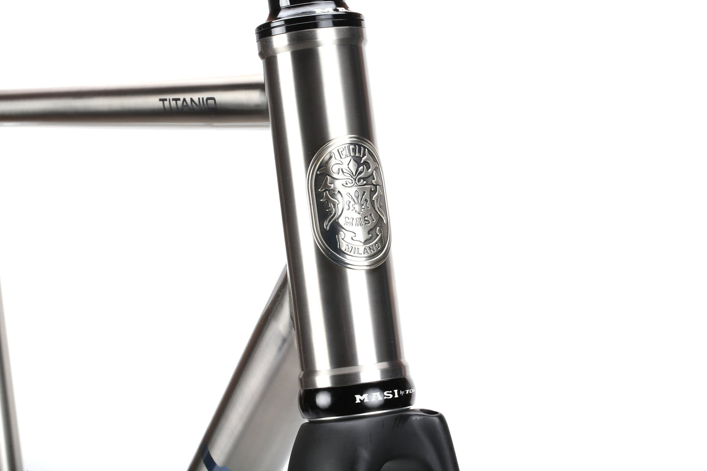 The Masi Bikes TITANIO FRAMESET features a close-up of a metallic bicycle frame with an intricate emblem and TITANIO engraving, showcasing polished metal tubing, 32c tire clearance, and exceptional craftsmanship.