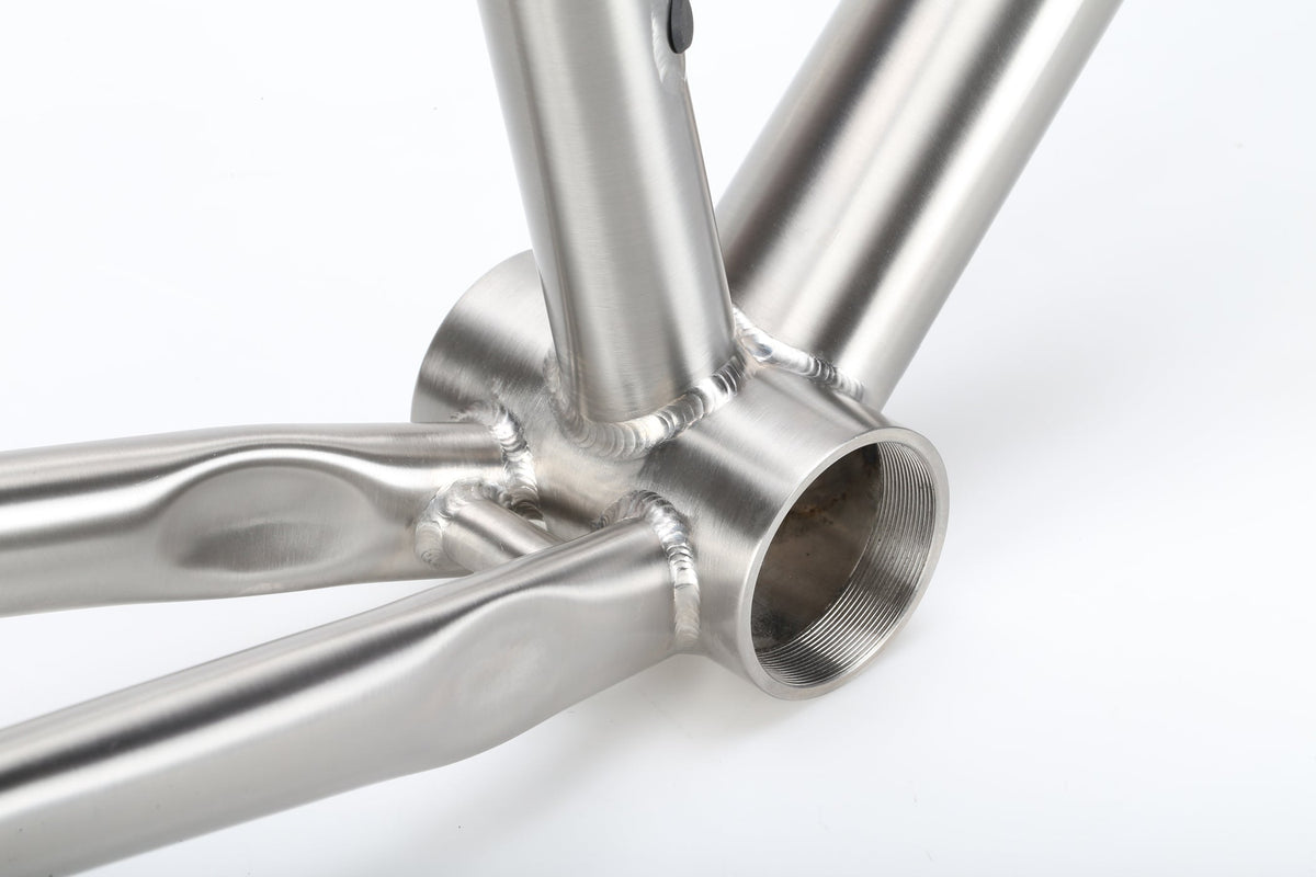 Close-up of the TITANIO FRAME’s titanium bottom bracket and welded joints against a white background.