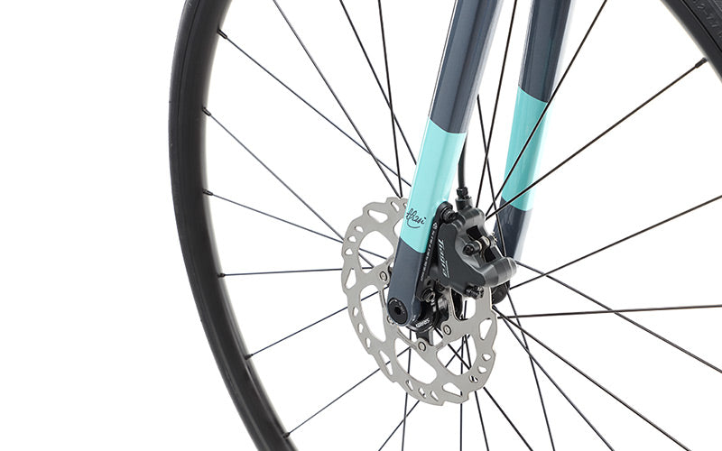Close-up of a VINCERE 3 bicycle front wheel by Masi Bikes, featuring a disc brake. The fork sports dark blue and mint green colors. Thin, evenly spaced spokes highlight its modern design, complemented by Shimano Tiagra components.
