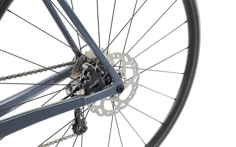 Close-up of a Masi Bikes VINCERE 3 bicycles rear wheel, featuring the Shimano Tiagra disc brake system and gear mechanism. Spokes and part of the alloy frame are visible, highlighting the intricate metal components.