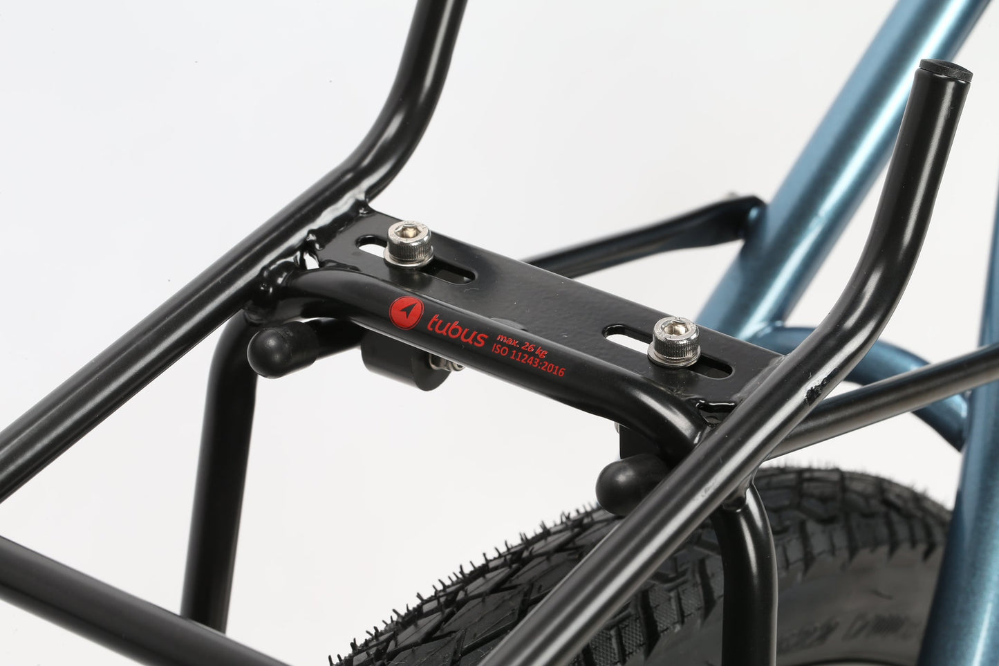 Close-up of a black Tubus bike rack, ideal for adventure and secured with bolts, mounted over the rear wheel of a Masi Bikes GIRAMONDO 700c. Designed for carrying bags or cargo, it features the red Tubus logo on its metallic blue frame.
