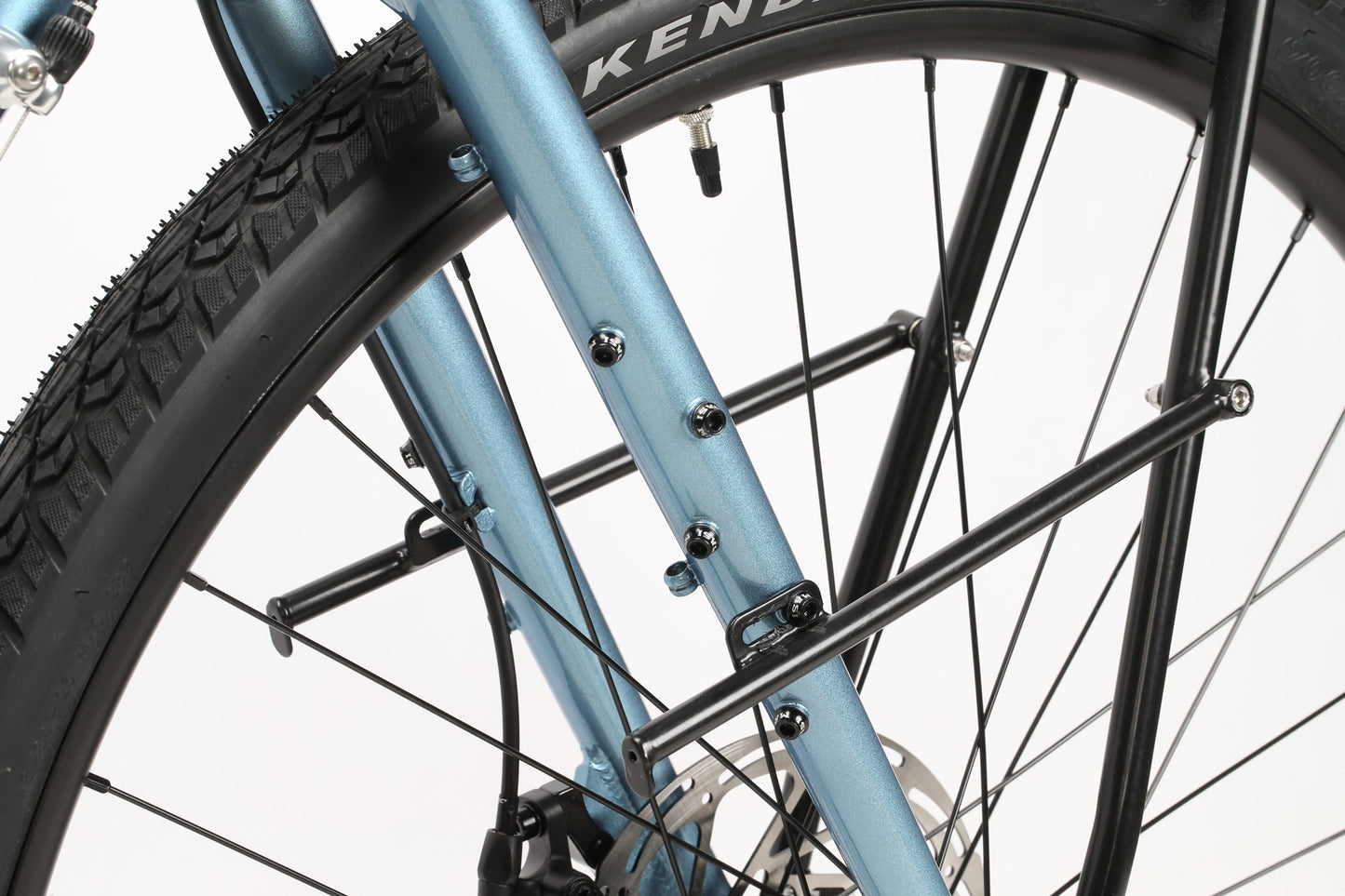 Close-up of the GIRAMONDO 700c by Masi Bikes featuring a light blue metallic frame, black KENDA tire, spokes, and a metal rack mount for adventure. The bike stands against a plain white background.