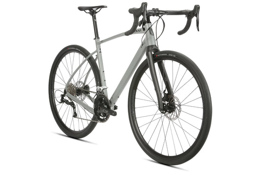 The BRUNELLO R10 is a sleek gray road bike with carbon fork, drop handlebars, black tires, and disc brakes, seen from the front.
