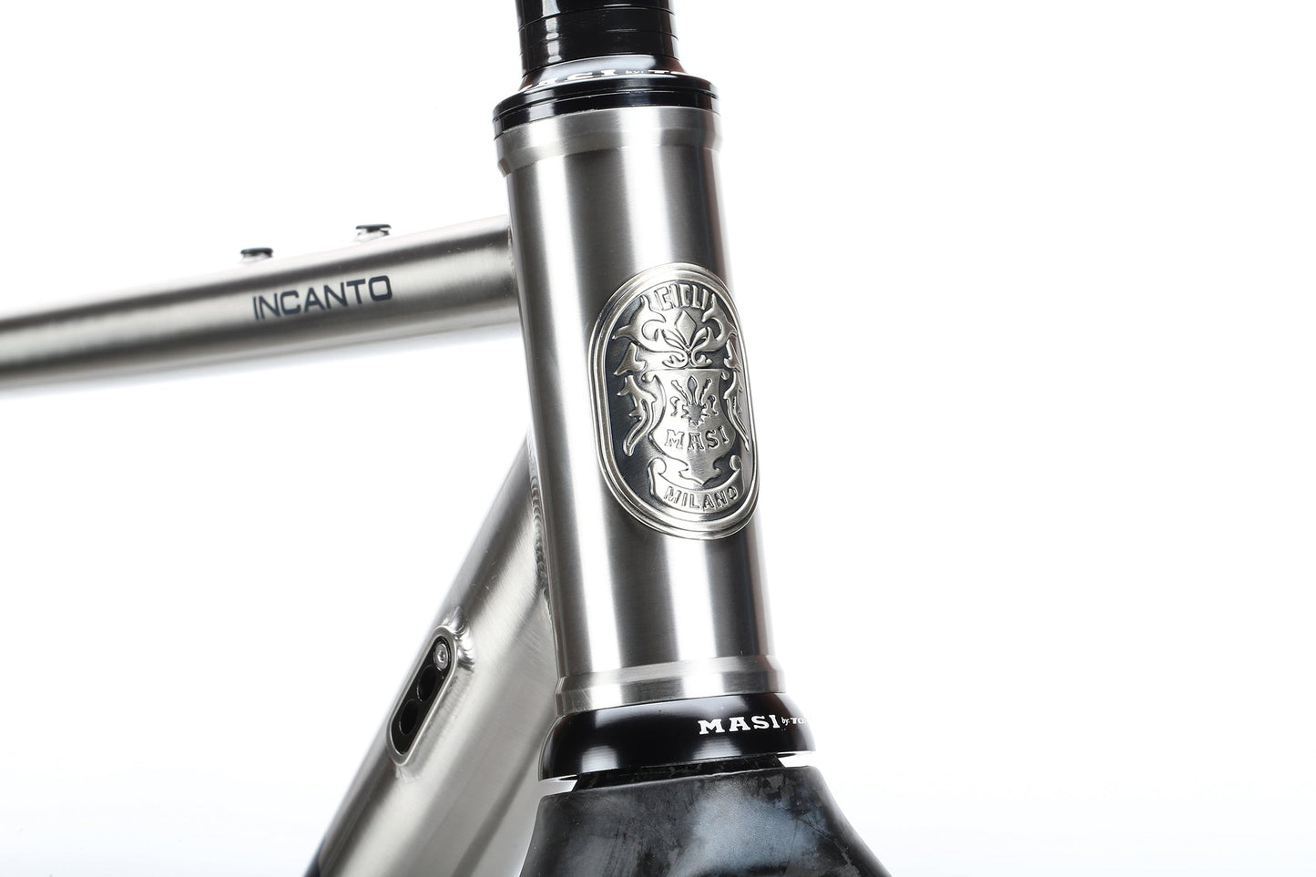 A close-up of the Masi Bikes INCANTO Ti FRAMESET reveals a sleek titanium gravel bike frame. It features an engraved emblem with intricate detailing at the front and INCANTO branded on the polished, metallic 3AL/2.5V tubing.