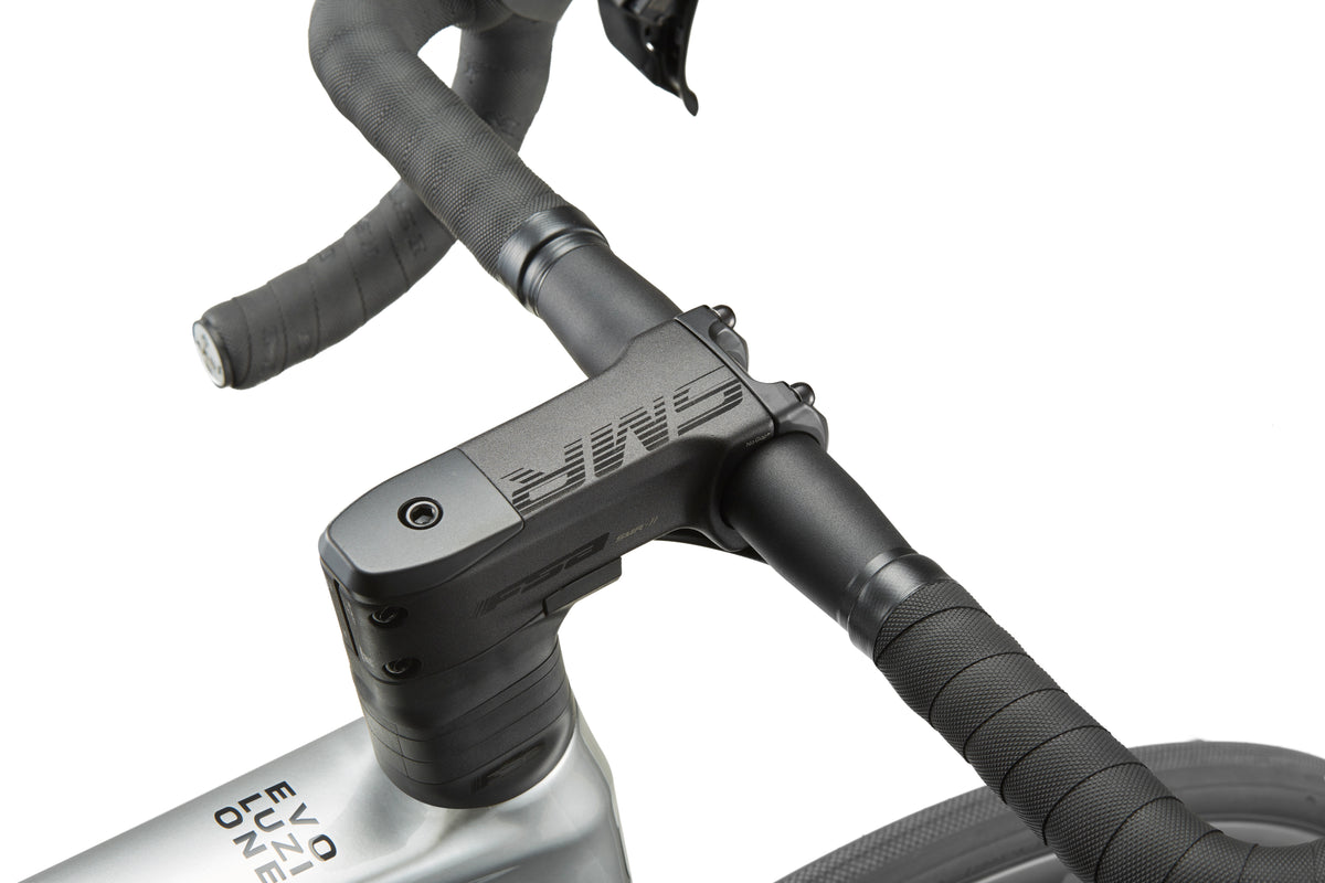 Close-up of a sleek road bike handlebar and stem with black tape and branding, hinting at the Masi EVOLUZIONE 1s metallic silver frame.