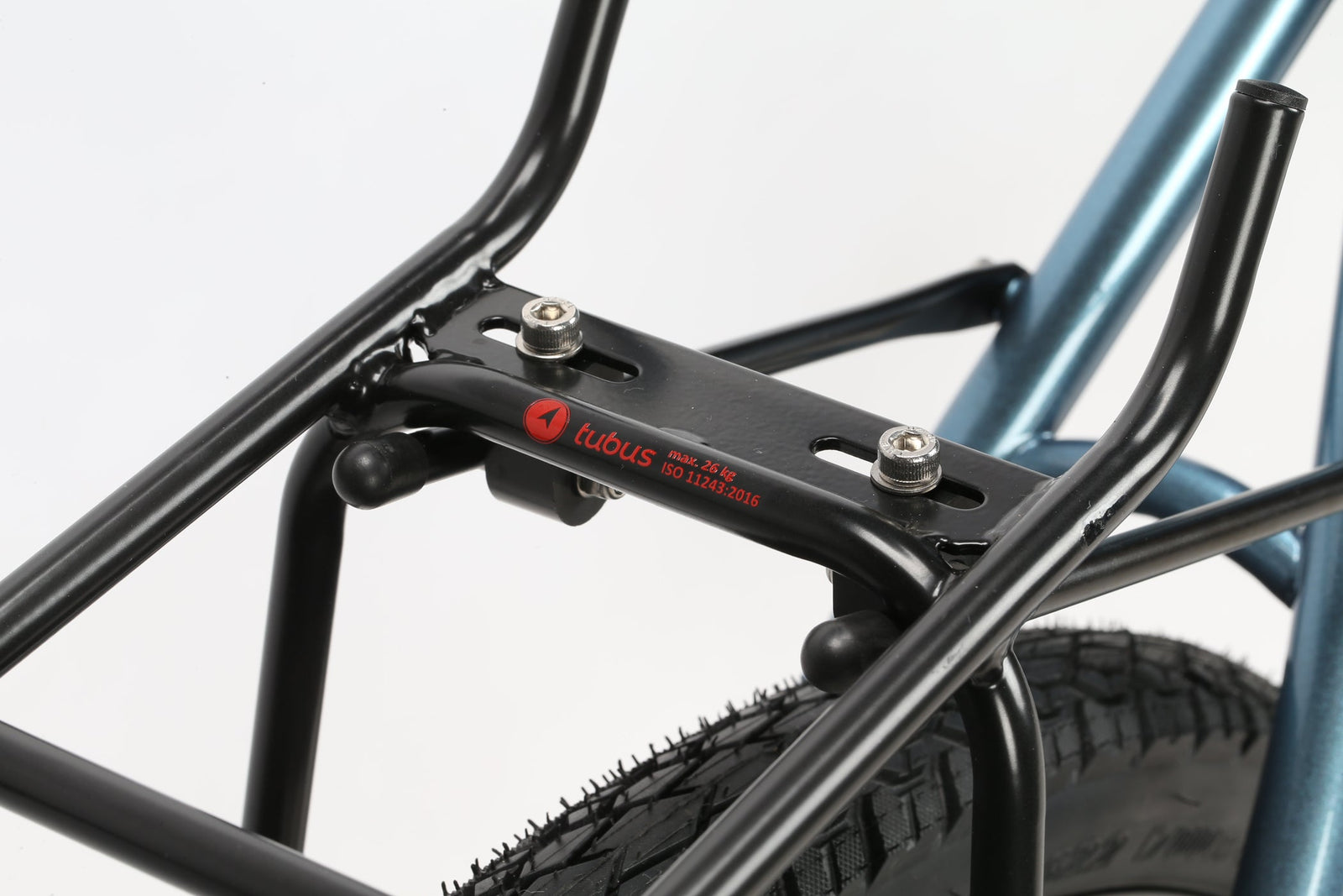 Close-up of a black Tubus bike rack, ideal for adventure and secured with bolts, mounted over the rear wheel of a Masi Bikes GIRAMONDO 700c. Designed for carrying bags or cargo, it features the red Tubus logo on its metallic blue frame.