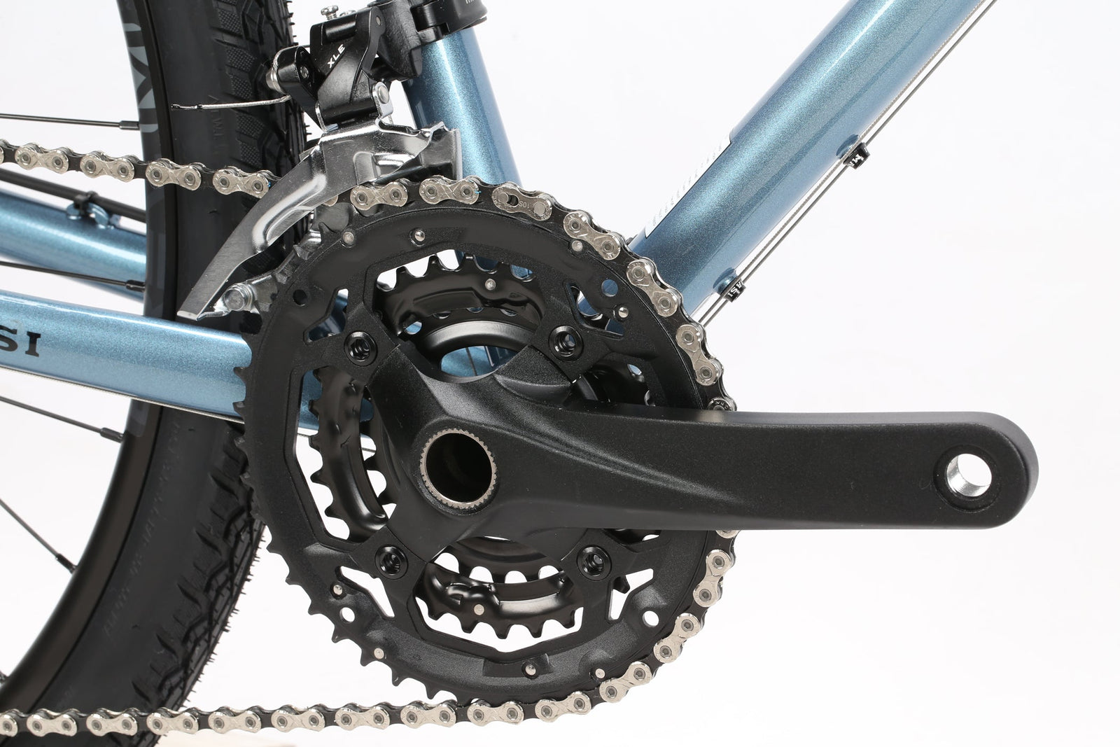 Close-up of a Masi Bikes GIRAMONDO 700c touring bikes drivetrain, showcasing a black crankset with chainrings and a silver chain on a light blue frame. The focus is on the gear mechanism, capturing adventures essence with the tires tread pattern hinting at its Giramondo legacy.