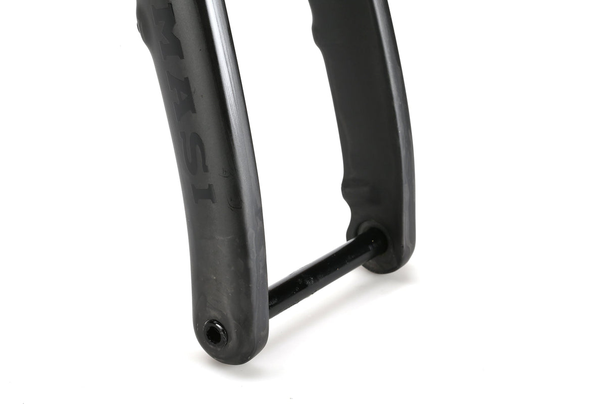 Close-up of titanium bicycle fork dropout with through axle on the Masi Bikes INCANTO Ti FRAMESET. The black fork has a slight sheen, features 3AL/2.5V tubing, and displays part of the brand name MASI. The cylindrical axle is centered on the gravel bikes frame.